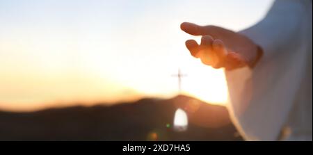 Mani di Gesù risorto dalla tomba e sfondo luminoso, cielo e croce amore e concetto di salvezza Foto Stock