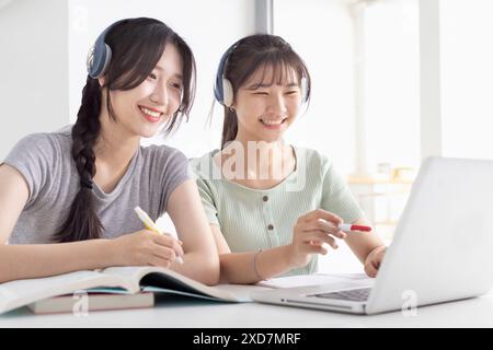 Ragazze felici con le cuffie wireless che leggono ascoltano i corsi online, studiano da casa Foto Stock