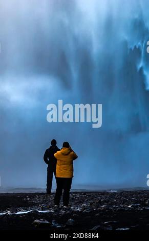 Un uomo e una donna stanno di fronte a una cascata, facendo una foto. La scena è serena e tranquilla, dato che la coppia gode della bellezza della natura Foto Stock