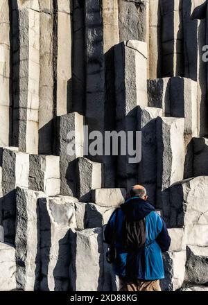 Un uomo è in piedi di fronte alle colonne di basalto Gardar, Islanda. Indossa una giacca blu e uno zaino. Concetto di avventura ed esplorazione Foto Stock