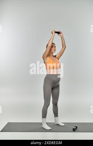 Una donna incinta in abbigliamento sportivo si erge su un tappetino da yoga con le mani alzate in aria, trasudando serenità e grazia. Foto Stock