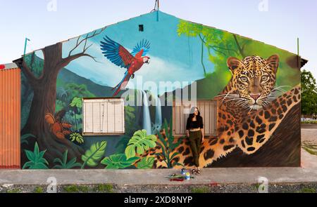 Donna che posa di fronte al murale della giungla con leopardo e macaw Foto Stock