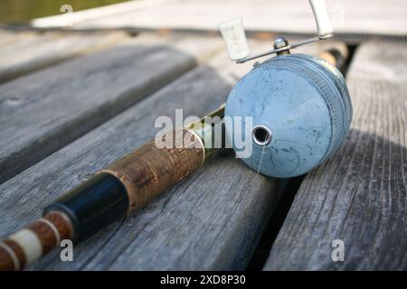 Primo piano di una canna da pesca d'epoca e di un rullo poggiati su una d di legno Foto Stock