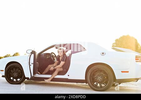 Giovane seduto in un'auto bianca con la porta aperta, a piedi nudi, S. Foto Stock