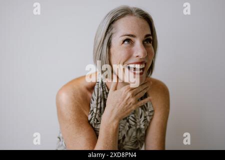 Donna lentigginita ridendo con capelli grigi in un outfit a motivi geometrici. Foto Stock