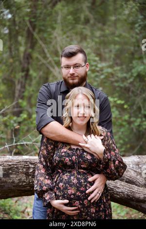 Una coppia incinta che abbraccia una foresta, con le braccia dell'uomo aro Foto Stock