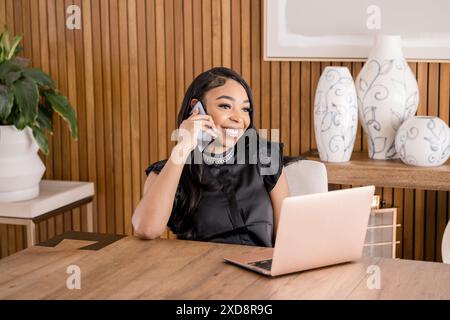 Donna sorridente e che lavora al computer portatile mentre parla al telefono Foto Stock