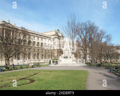 Statua in un parco con edificio storico e persone sedute sulle panchine Foto Stock