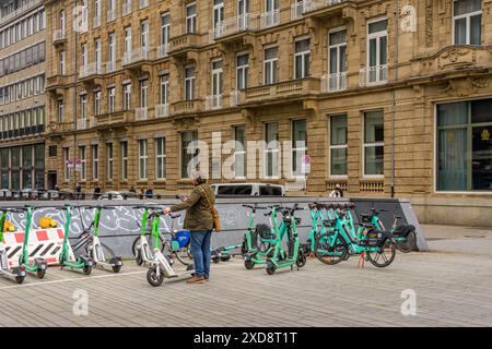 8 maggio 2024 - Düsseldorf, Germania: Uomo d'affari che usa lo smartphone per noleggiare uno scooter elettrico. Trasporti ecologici. Foto Stock
