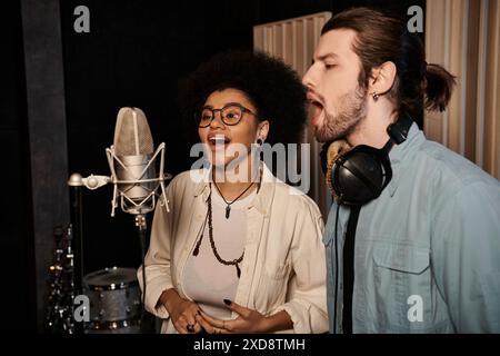 Un uomo e una donna cantano appassionatamente nei microfoni in uno studio di registrazione, circondati da strumenti musicali. Foto Stock