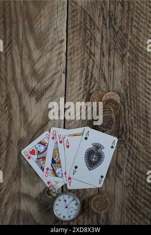 Una mano da poker che gioca a carte, un asso di picche sulla parte superiore, con orologio da tasca e monete poste accanto a loro su un vecchio tavolo in legno. Foto Stock