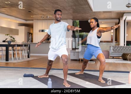 Pratica yoga insieme, giovane coppia in posa guerriera sui tappetini a casa Foto Stock