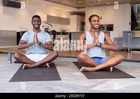 Pratica yoga insieme, giovane coppia seduta a gambe incrociate sui tappetini in soggiorno Foto Stock