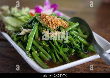 Mescolare la gloria cinese dell'acqua al mattino o gli spinaci dell'acqua con pasta di soia, un semplice piatto thailandese-cinese chiamato pad pak boong, servito su una porzione bianca Foto Stock