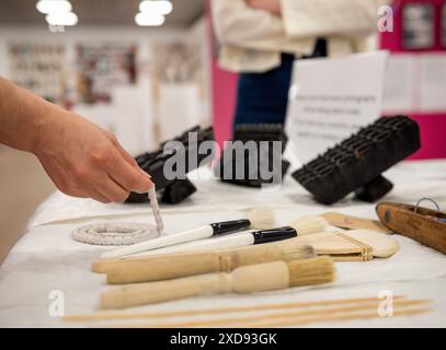 Una mano tiene una spazzola accanto a un tessuto del museo in una mostra di conservazione degli scialli Foto Stock