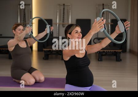 Due donne incinte che fanno yoga. Esercizi con un circolo ginnastico per Pilates. Foto Stock