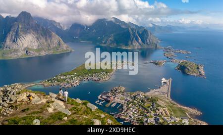 Una vista aerea di un fiordo norvegese, che mostra una piccola città annidata tra le montagne e l'acqua. Un paio di uomini e donne a Reinebringen Lofoten Norvegia Foto Stock