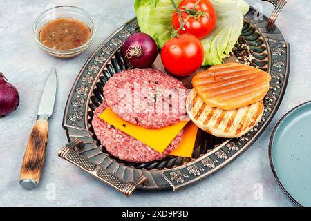 Hamburger freschi, formaggio, verdure e panini per cucinare. Cotolette di bistecca crude con carne macinata. Foto Stock