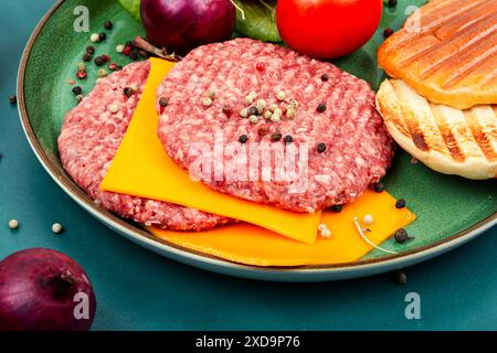 Hamburger crudi fatti in casa o hamburger, formaggio, verdure e panini per cucinare. Foto Stock