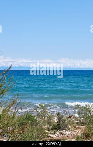 Costa selvaggia della costa meridionale del grande lago Issyk-Kul, vacanze estive in Kirghizistan. Cielo azzurro, acqua di stagno color smeraldo, piccola onda. Kirgiziy Foto Stock