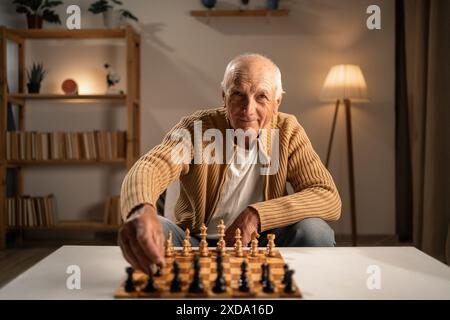 Uomo anziano che gioca a scacchi a casa la sera. Concetto di stile di vita in età di anzianità. Foto Stock