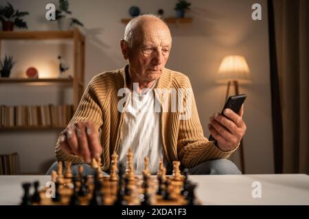 Uomo che gioca a scacchi studiando online sul cellulare Foto Stock