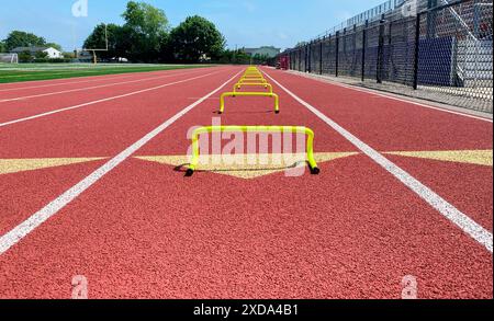 Visuale ad angolo basso di molti mini ostacoli gialli a banana allineati in una corsia su una pista per permettere ai corridori di correre in allenamento. Foto Stock