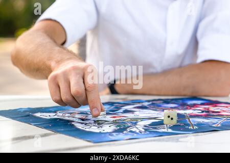 Rolling dice e Moving Game Chip: Primo piano delle mani dell'uomo sul tabellone dell'antico gioco indiano Leela, Turchia, Alanya - 14 aprile 2024 Foto Stock