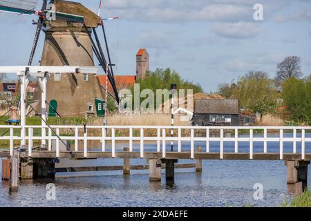 Mulino a vento e ponte su un fiume in un villaggio idilliaco con una piccola casa e alberi, kinderdijk, paesi bassi Foto Stock