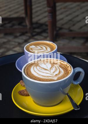 Due tazze di cappuccino in tazze colorate: Blu e giallo su un tavolo basso con latte art Foto Stock