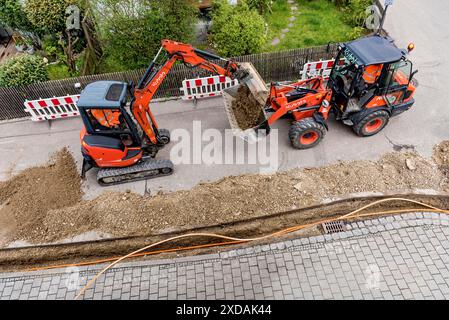 Operai edili che posa cavi in fibra ottica in trincee sotto asfalto, trincee, escavatore, pala gommata, cantiere edile, fibra ottica Foto Stock