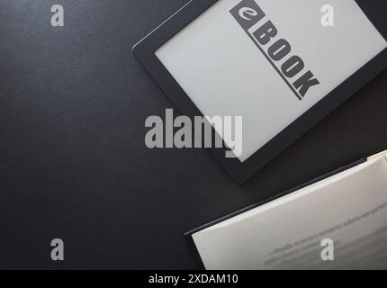 Dettaglio dell'eBook con testo scritto sullo schermo isolato su un tavolo nero con un tradizionale libro cartaceo. Concetto di lettura in un libro elettronico. vista dall'alto Foto Stock