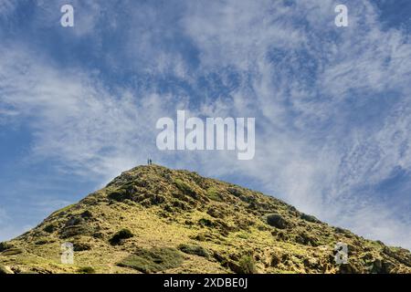 Due escursionisti in cima al Morro de Tramuntana a Minorca, con una vista mozzafiato sull'aspra collina e un vivace cielo blu pieno di nuvole. Foto Stock