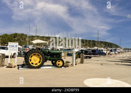 Vista di Puerto de Addaya Marina a Minorca con un classico trattore verde, auto parcheggiate e numerose barche a vela attraccate nel porto sotto un luminoso Foto Stock