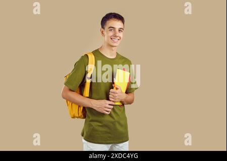 Ritratto di un bel sorridente ragazzo adolescente che posa con lo zaino che tiene in mano i notebook. Foto Stock