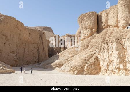 Tre persone in abiti moderni sono nanizzate dalle aride scogliere calcaree della Valle dei Re, Luxor, Egitto. Foto Stock