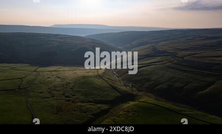 Questa immagine cattura un fiume che si snoda attraverso una lussureggiante valle verde con colline circostanti sotto un vasto cielo all'alba o al tramonto Foto Stock