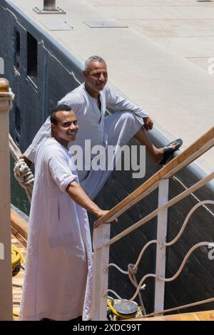 Due membri dell'equipaggio egiziano vestiti in modo tradizionale di una barca a vela Lazul dahabiya osservano mentre aspettano che le acque si alzino nella chiusa di Esna. Foto Stock