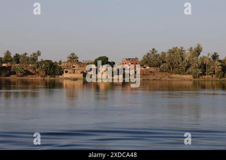 Due egiziani regnano una barca tradizionale lungo le acque tranquille del Nilo nel tardo pomeriggio di fronte a un villaggio tra Luxor ed Esna. Foto Stock