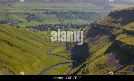 Un paesaggio lussureggiante che cattura l'essenza di Arncliffe con il suo tortuoso fiume attraverso la verde valle, incorniciata da pendii e ombre alla luce del sole Foto Stock