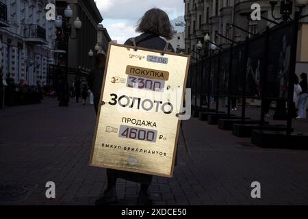 Mosca, Russia. 21 giugno 2024. Una donna possiede un banner pubblicitario che mostra informazioni sui prezzi per la vendita e l'acquisto di oro in via Arbat, situata nel cuore di Mosca, Russia. Foto Stock