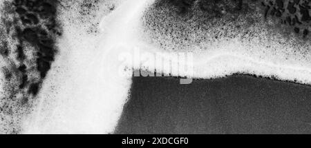 Una fotografia in bianco e nero che raffigura le onde schiumose dell'oceano su una spiaggia sabbiosa. L'immagine acquisisce un pattern astratto dinamico creato b Foto Stock