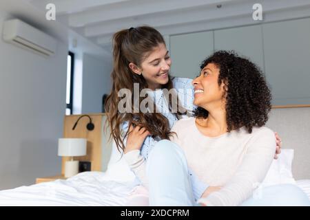 sorrisi indefiniti, seduti su un letto, godendosi il tempo insieme a casa Foto Stock