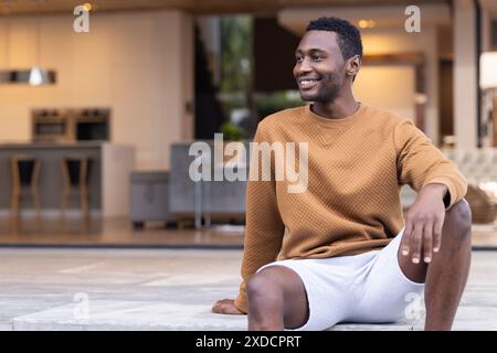 Seduti sui gradini, uomo in abiti casual e pantaloncini bianchi sorridenti e distanti lo sguardo, copia spazio Foto Stock