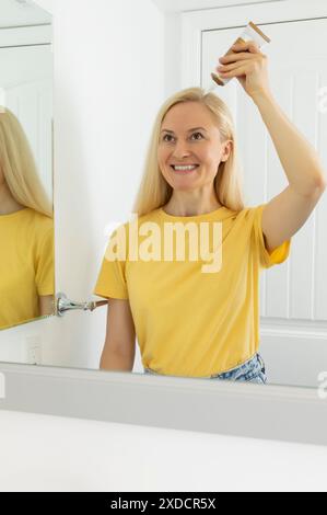 La donna caucasica di mezza età applica peeling del cuoio capelluto, scrub sulla pelle della testa, capelli. Fora. La femmina bianca bionda contiene la provetta con purificazione e lenizione Foto Stock