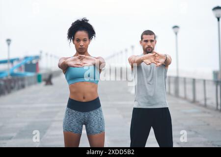 Coppia, braccia all'aperto e stretching per il riscaldamento, corridori e allenamenti sul lungomare per il fitness. Persone, supporto e flessibilità per muscoli o atleti Foto Stock