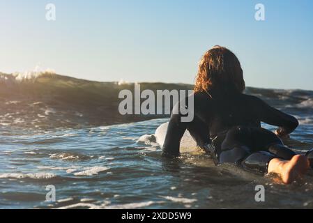 Schiena, sport e uomo in oceano per surf, remare ed equilibrio per professionisti in allenamento. Spiaggia, acqua e onde con surfista maschile per il fitness Foto Stock