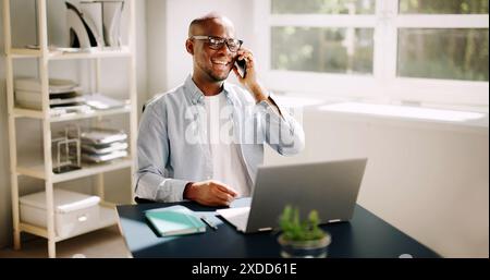Felice uomo d'affari afroamericano che effettua una chiamata virtuale dalla scrivania dell'ufficio domestico, dimostrando la flessibilità del lavoro remoto. Foto Stock