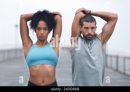 Coppia, braccia all'aperto e stretching per sport, runner e allenamenti sul lungomare per il fitness. Persone, supporto e flessibilità per muscoli o atleti Foto Stock