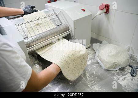Il lavoratore srotola un pezzo di impasto in una macchina per lenzuola Foto Stock
